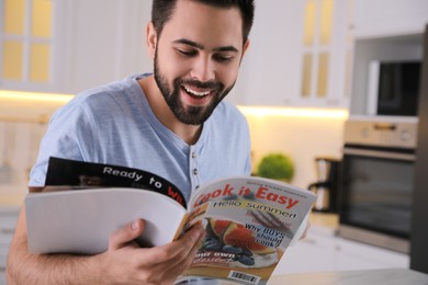 Photo of Young man with cup of drink reading magazine at table in kitchen