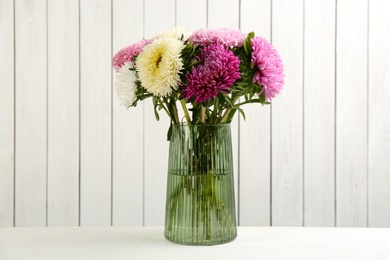 Beautiful asters in vase on table against white wooden background. Autumn flowers