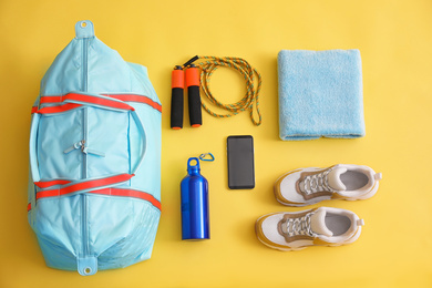 Photo of Gym bag, smartphone and sports equipment on yellow background, flat lay