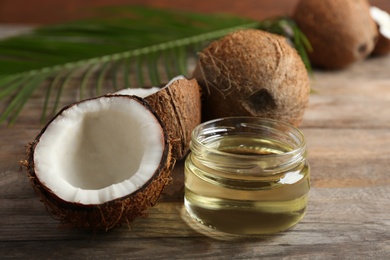 Photo of Jar of natural organic oil and coconuts on brown wooden table, closeup
