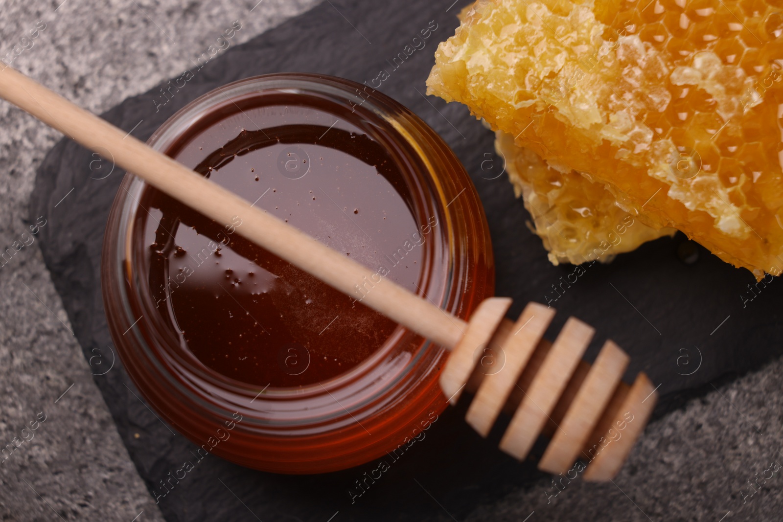 Photo of Sweet golden honey in jar, dipper and pieces of honeycomb on grey table, top view