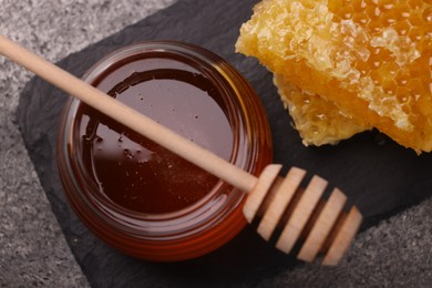 Sweet golden honey in jar, dipper and pieces of honeycomb on grey table, top view