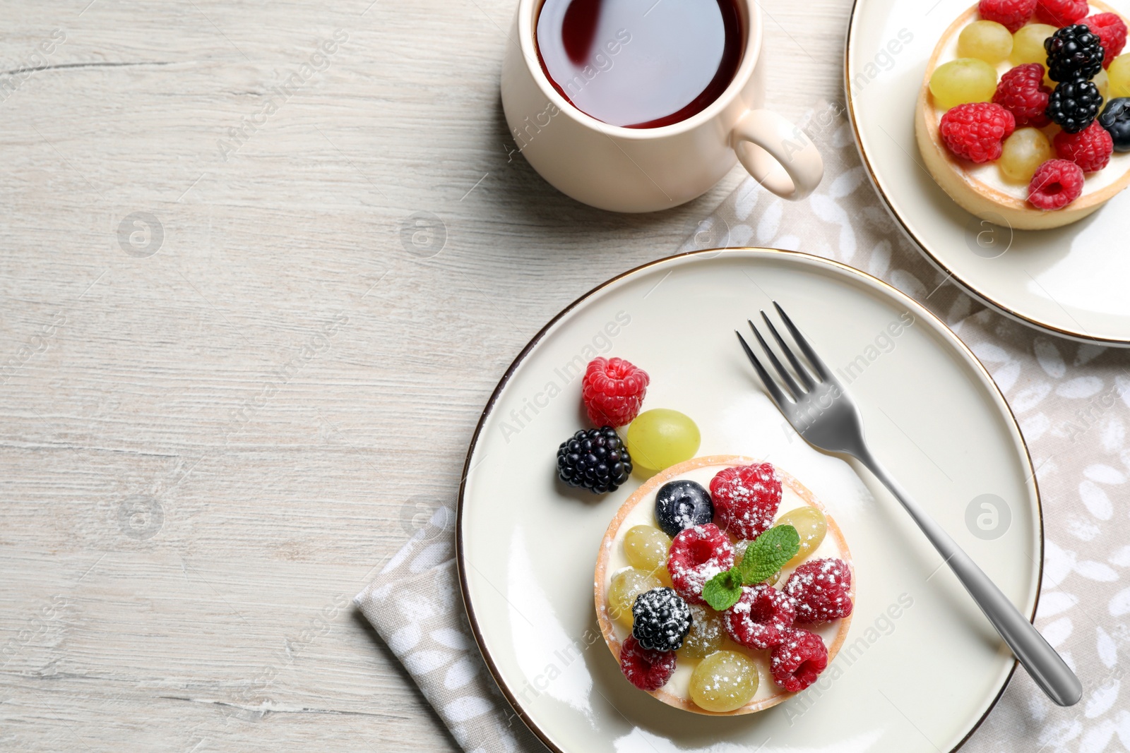 Photo of Delicious tartlets with berries and tea on light wooden table, flat lay. Space for text