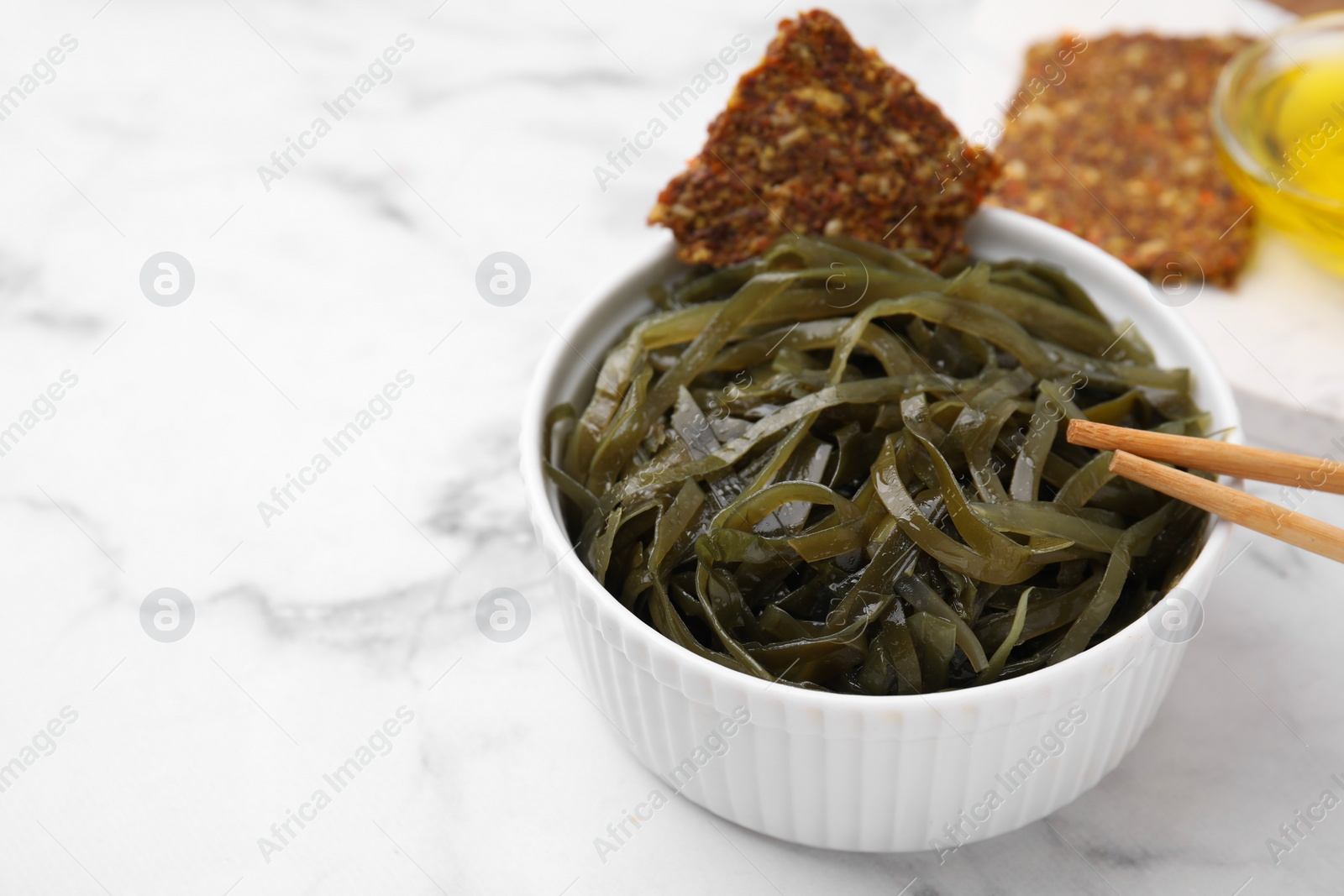 Photo of Tasty seaweed salad in bowl served on white marble table, closeup. Space for text