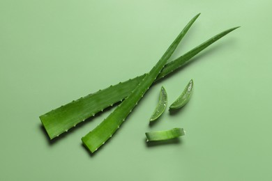 Photo of Cut aloe vera leaves on light green background, flat lay