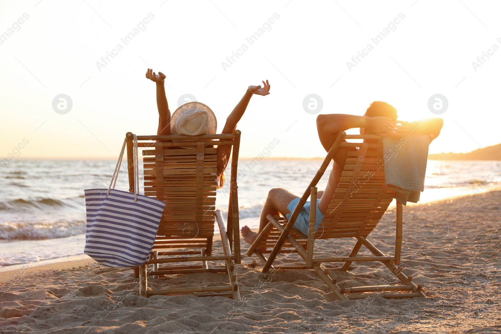 Photo of Young couple relaxing in deck chairs on beach near sea