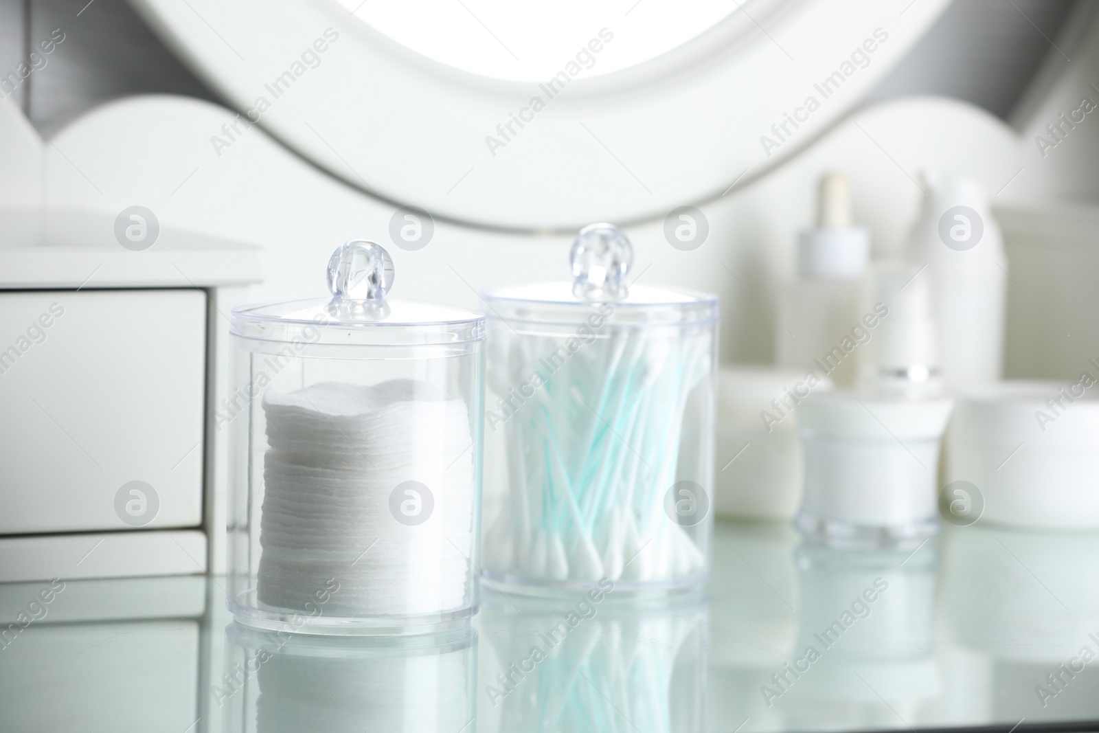 Photo of Containers with cotton swabs and pads near cosmetic products on dressing table