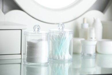 Containers with cotton swabs and pads near cosmetic products on dressing table