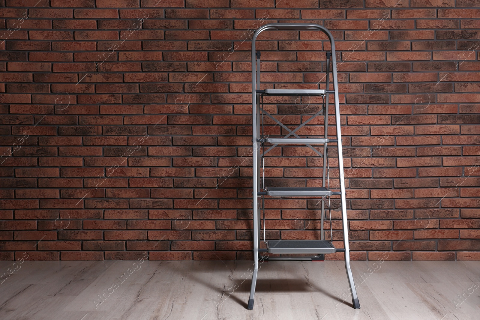 Photo of Modern metal stepladder near brick wall indoors. Space for text