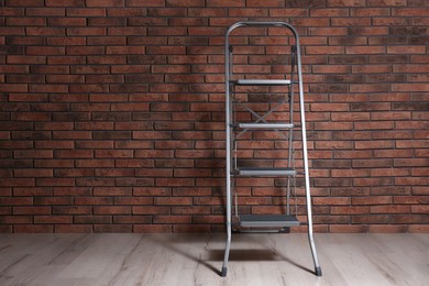 Photo of Modern metal stepladder near brick wall indoors. Space for text