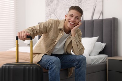 Smiling guest with suitcase on bed in stylish hotel room