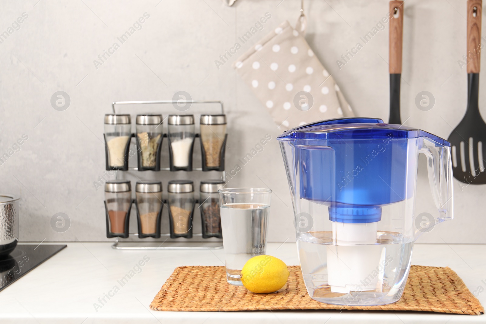 Photo of Water filter jug, glass and lemon on white countertop in kitchen