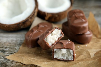 Photo of Delicious milk chocolate candy bars with coconut filling on wooden table, closeup