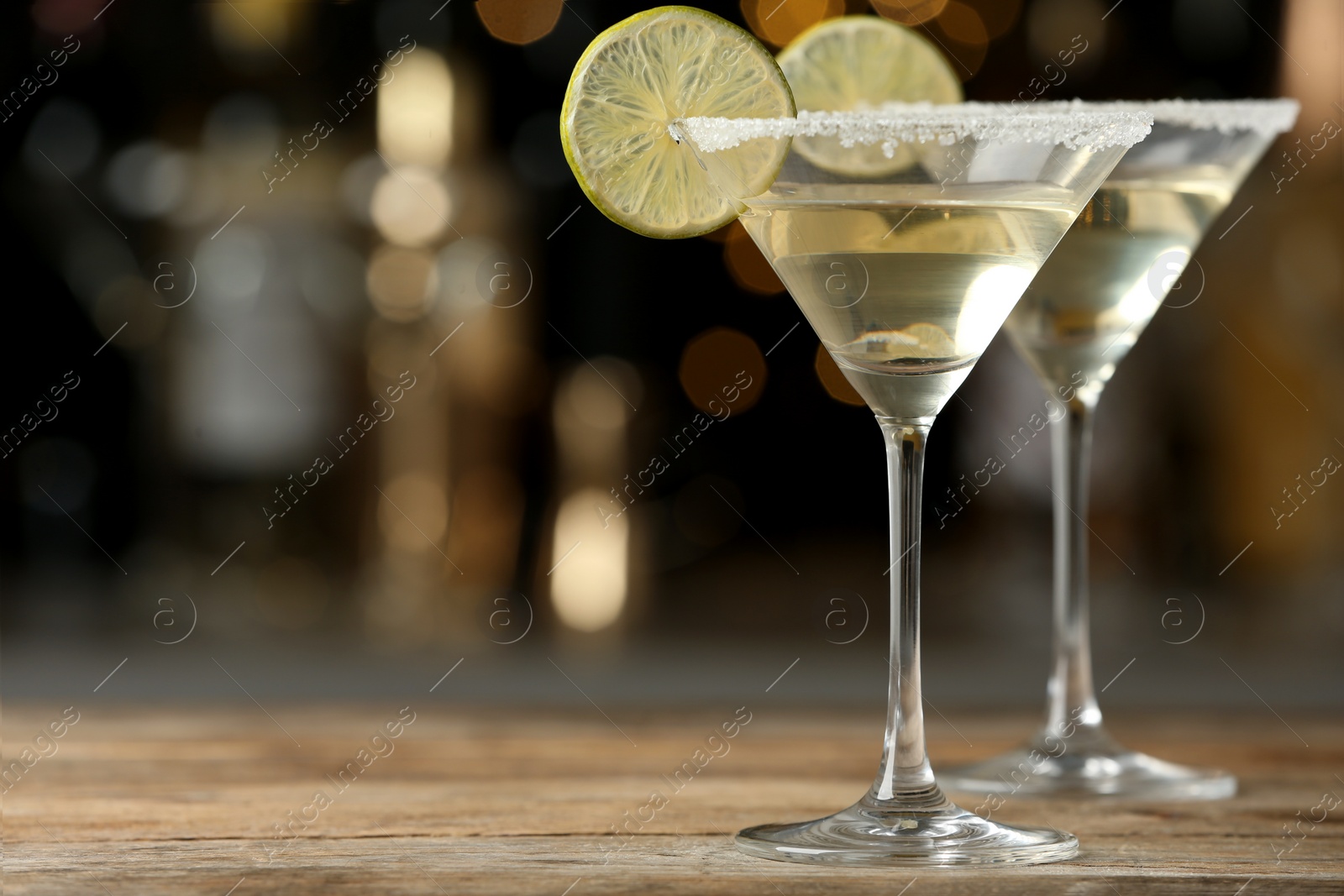 Photo of Glasses of Lime Drop Martini cocktail on wooden table against blurred background. Space for text