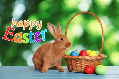 Image of Happy Easter. Adorable bunny and wicker basket with eggs on wooden table outdoors