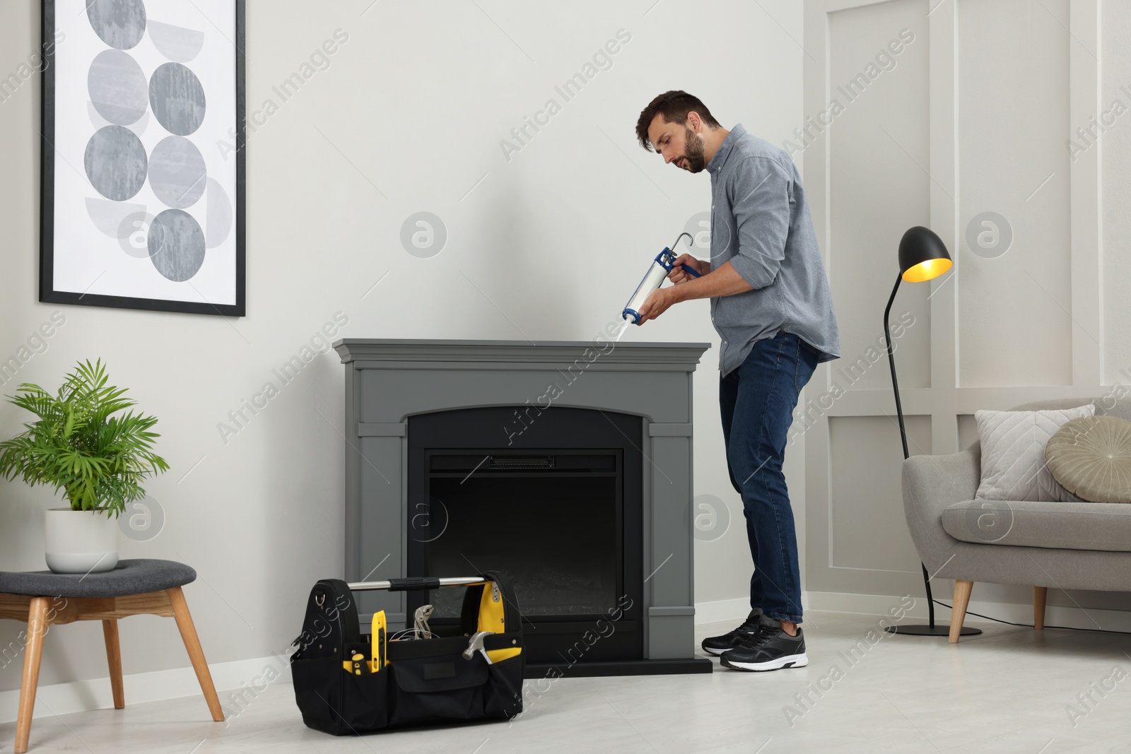 Photo of Man sealing electric fireplace with caulk near wall in room