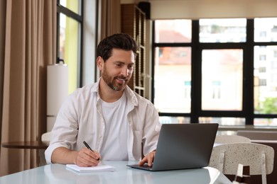 Photo of Man working on laptop and writing something at table in cafe