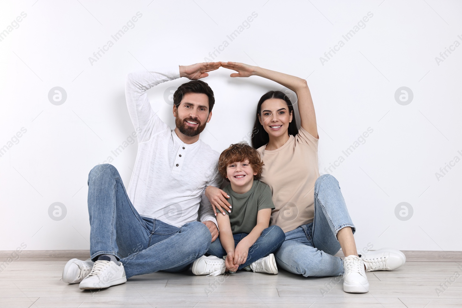 Photo of Family housing concept. Happy woman and her husband forming roof with their hands while sitting with son on floor at home