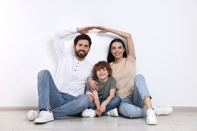 Photo of Family housing concept. Happy woman and her husband forming roof with their hands while sitting with son on floor at home