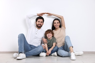 Family housing concept. Happy woman and her husband forming roof with their hands while sitting with son on floor at home