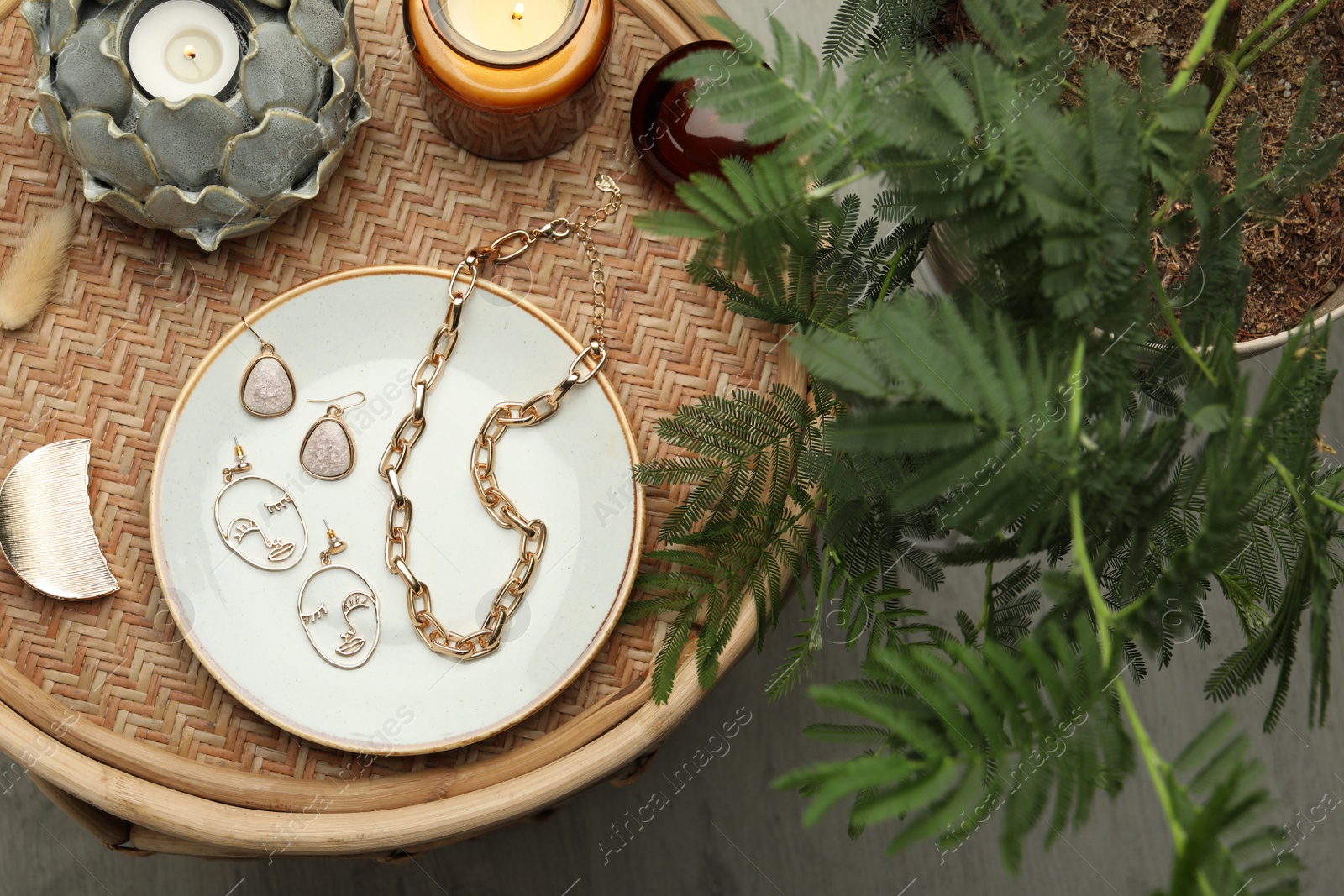 Photo of Stylish golden bijouterie and candles on wicker table, top view