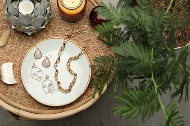 Photo of Stylish golden bijouterie and candles on wicker table, top view