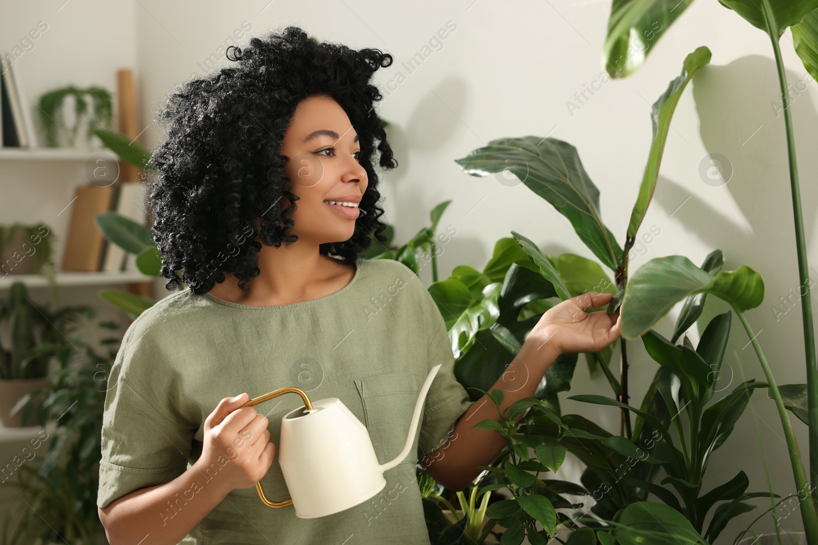 Photo of Happy woman watering beautiful potted houseplants indoors