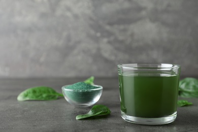 Photo of Glass of spirulina drink, spinach and powder on table against grey background. Space for text