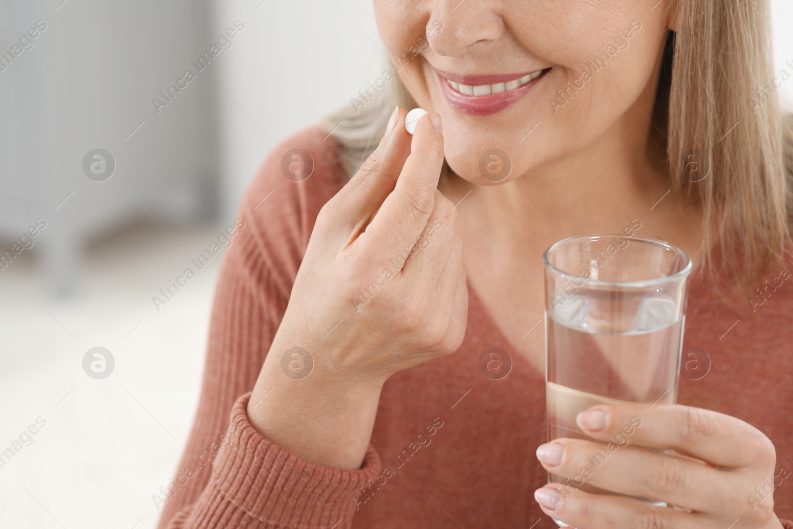 Photo of Senior woman with glass of water taking pill indoors, closeup