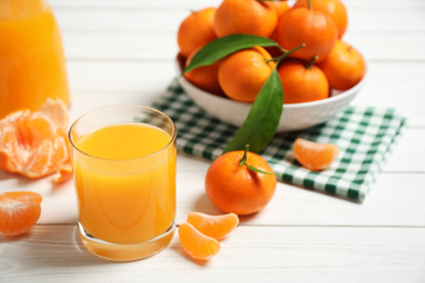 Glass of fresh tangerine juice and fruits on white wooden table