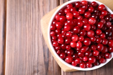 Photo of Fresh ripe cranberries in bowl on wooden table, top view. Space for text