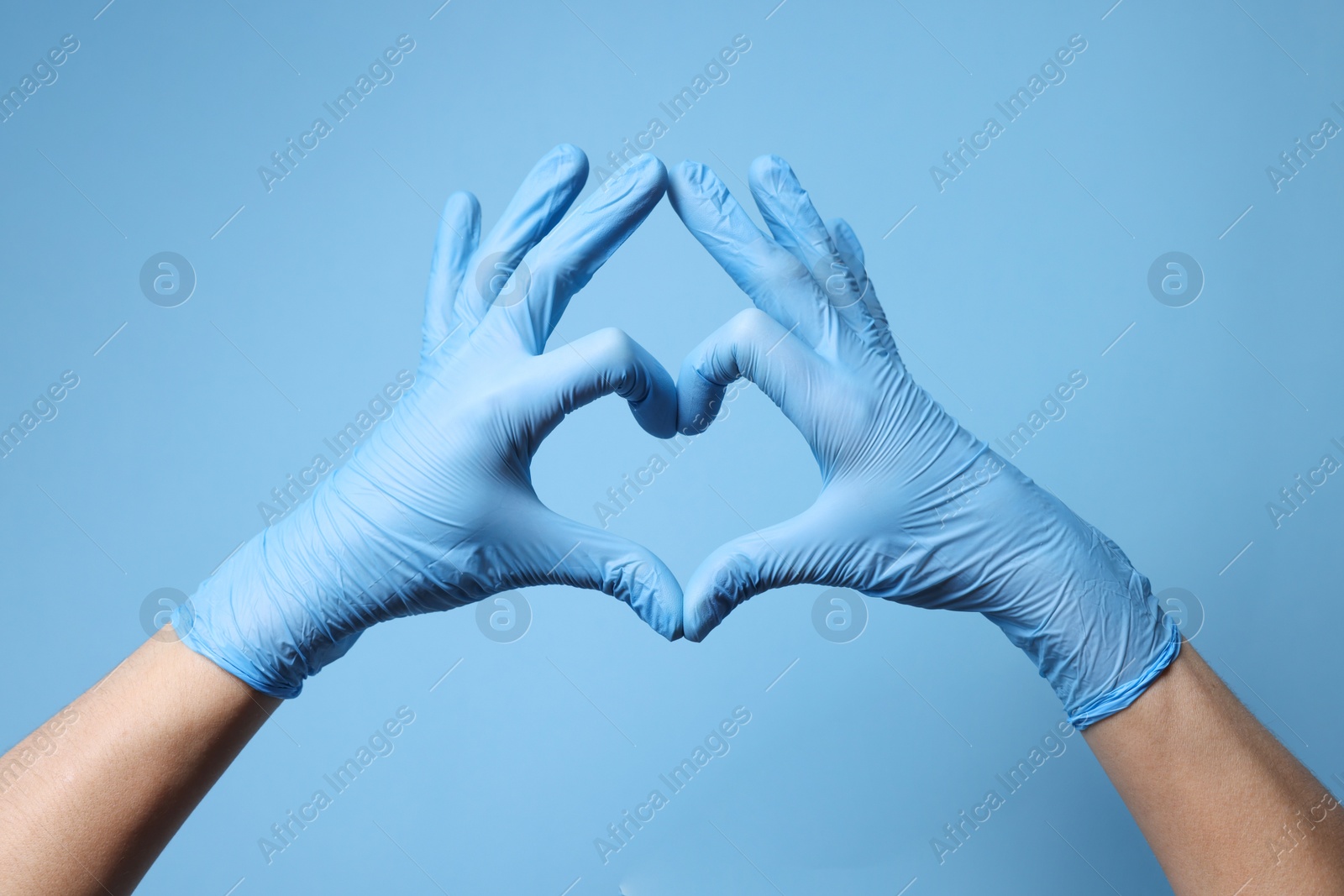 Photo of Doctor wearing medical gloves making heart gesture on light blue background, closeup