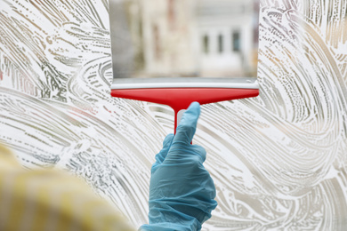 Woman cleaning window with squeegee indoors, closeup