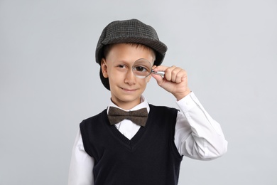 Cute little detective with magnifying glass on grey background