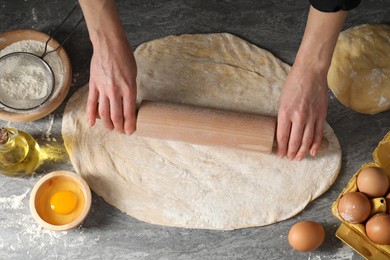 Photo of Woman rolling raw dough at grey table, closeup