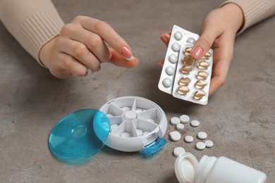 Woman putting pill into plastic box at grey table, closeup