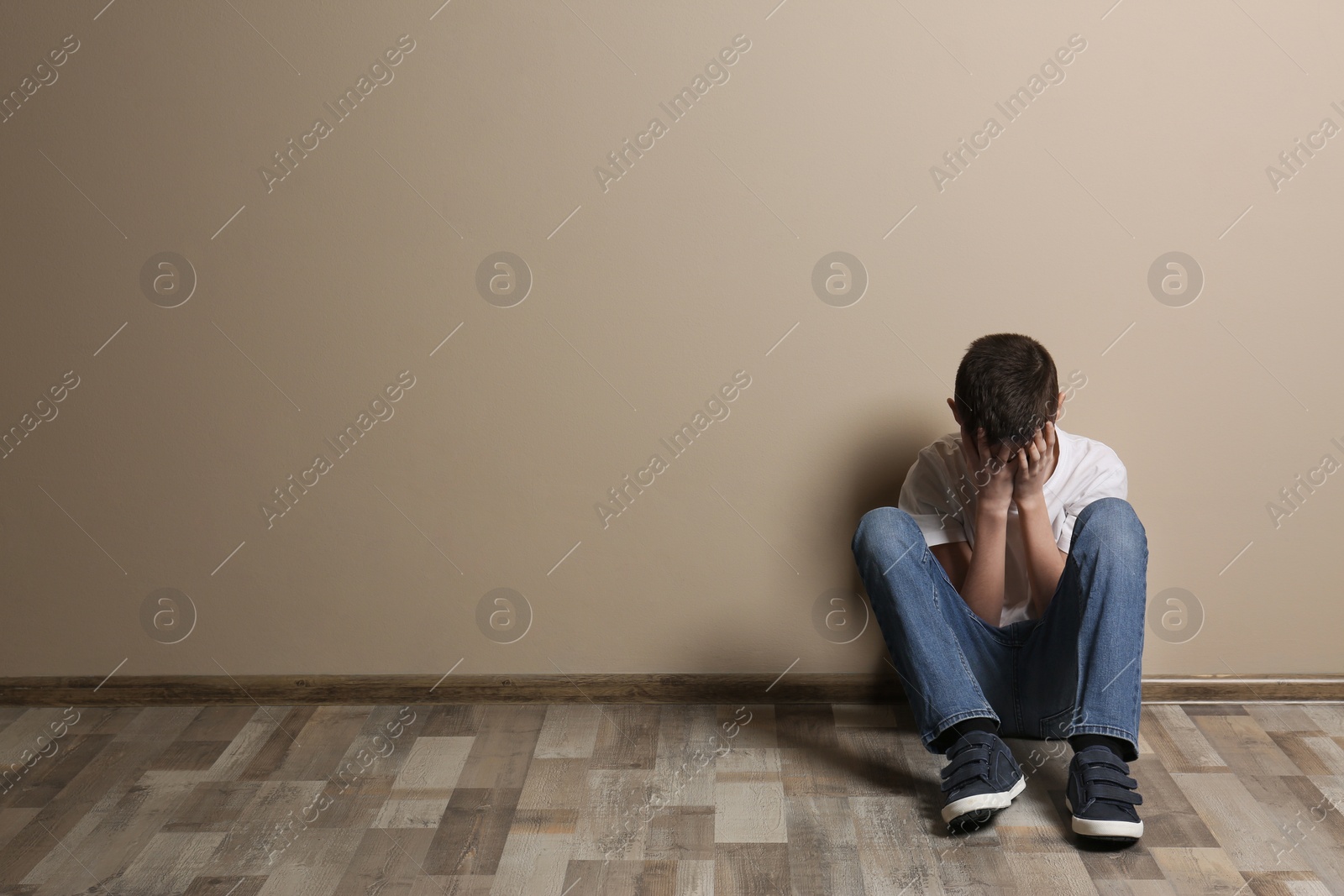 Photo of Upset boy sitting on floor at color wall. Space for text