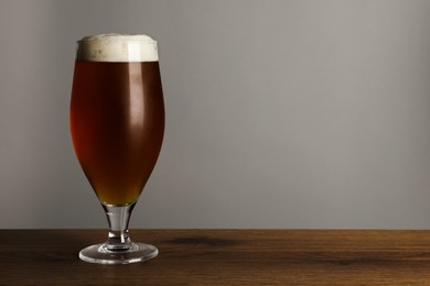 Glass of tasty dark beer on wooden table against grey background. Space for text