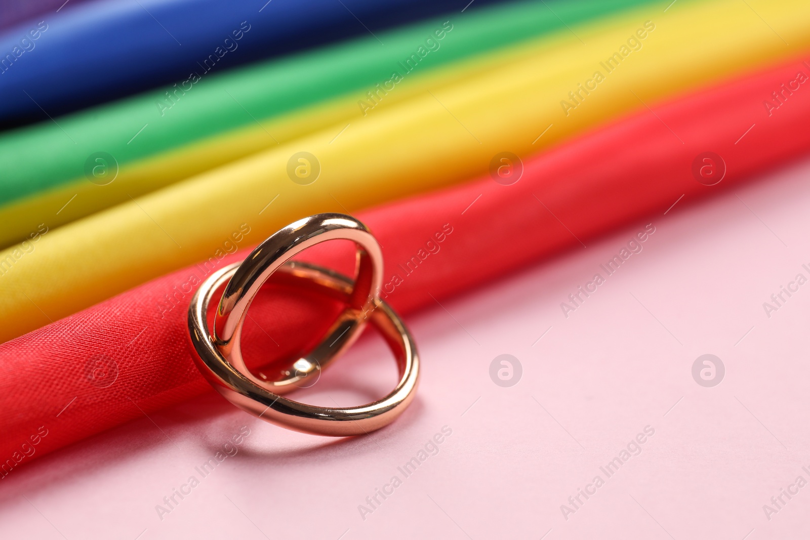 Photo of Rainbow LGBT flag and wedding rings on pink background, closeup