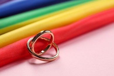 Rainbow LGBT flag and wedding rings on pink background, closeup