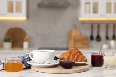 Photo of Breakfast served in kitchen. Fresh croissant, coffee, jam, honey and sweetened condensed milk on white table