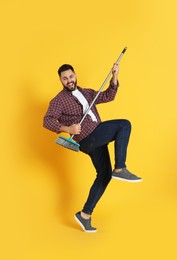Young man with broom having fun on orange background