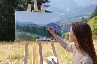 Photo of Young woman drawing on easel in mountains