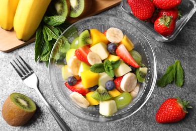Delicious fresh fruit salad in bowl on grey table, flat lay