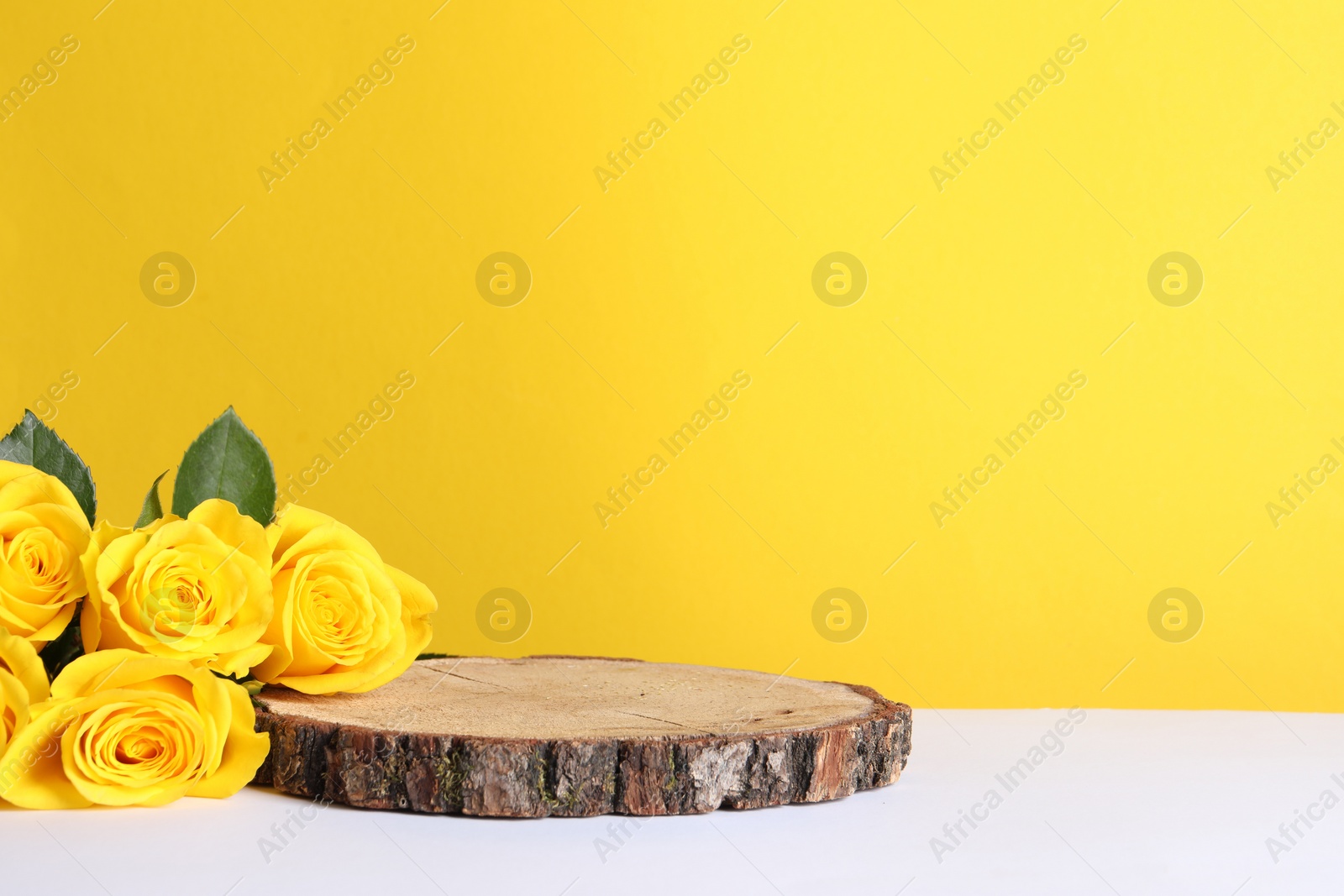 Photo of Beautiful presentation for product. Wooden stump and roses on white table against yellow background, space for text