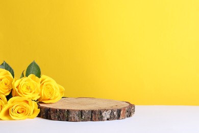 Beautiful presentation for product. Wooden stump and roses on white table against yellow background, space for text