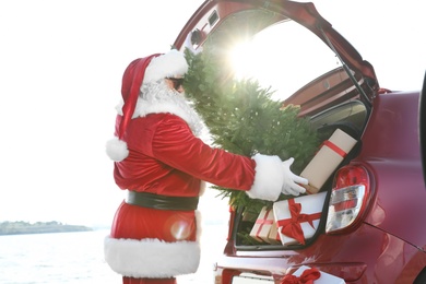 Authentic Santa Claus putting gift boxes and Christmas tree into car trunk, outdoors