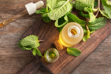 Bottles of essential oil and mint leaves on wooden background