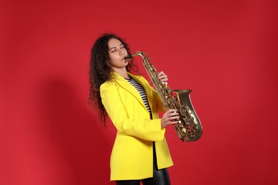 Photo of Beautiful African American woman playing saxophone on red background