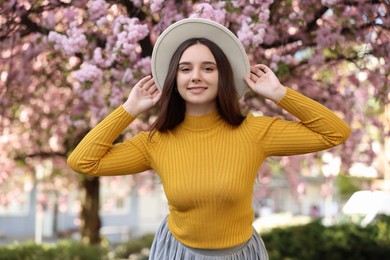 Beautiful woman in hat near blossoming tree on spring day